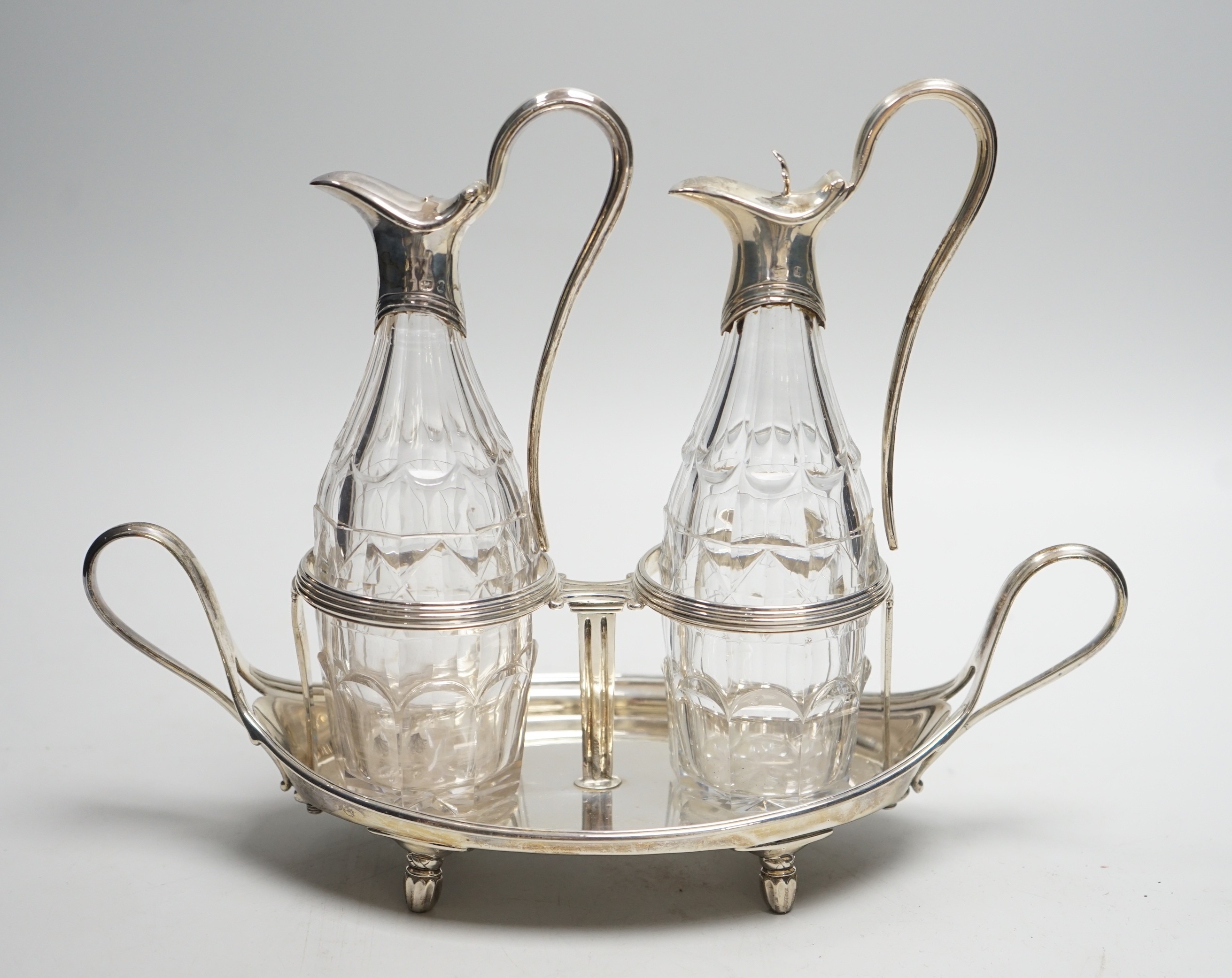 A George III silver navette shaped two handled oil and vinegar stand, with two matching silver mounted cut glass bottles (one thumbpiece missing), John Scofield, London, 1787, length 28cm, stand, 13.7oz.